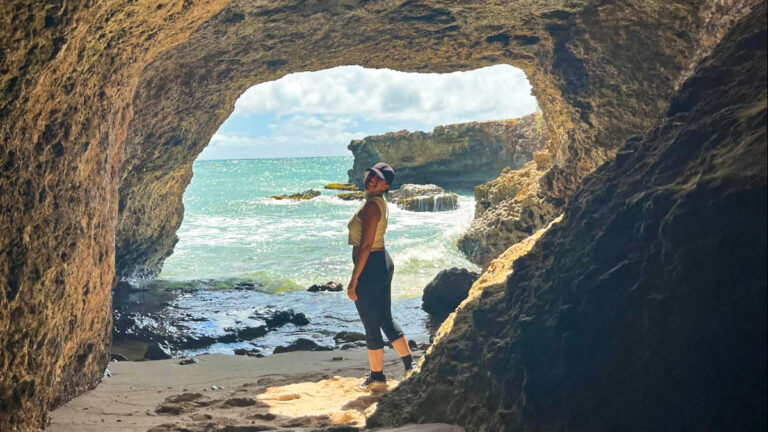The author Vanessa Ramos, posing for a photo at the cave with beach views in the background