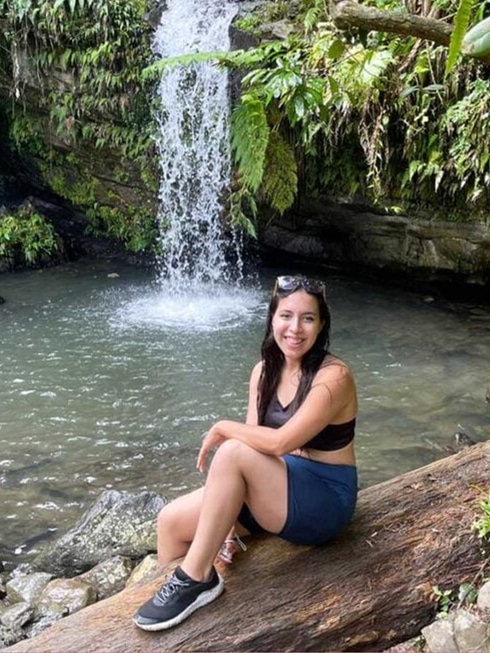Vanessa Ramos smiling for a photo with a waterfalls on her background in El Yunque