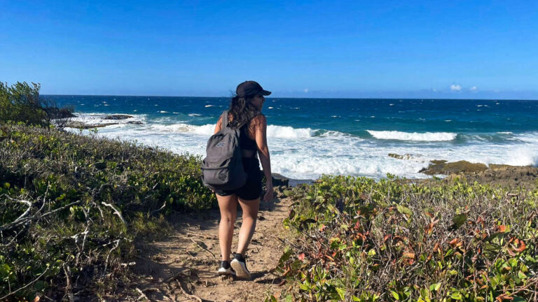 The author Vanessa Ramos, walking with her backpack on the pathway leading to the beach
