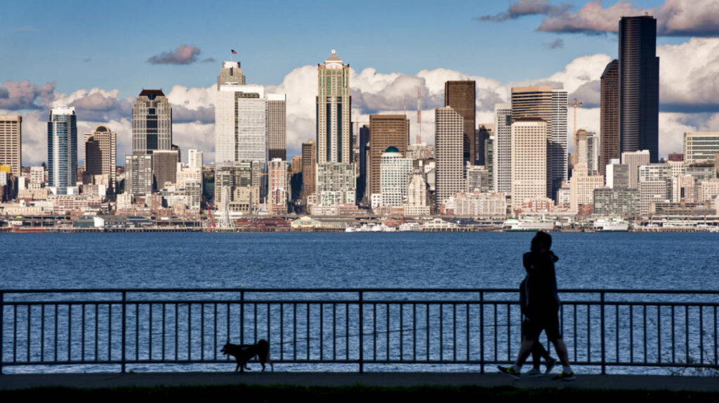 A silhouette of two people and their dog walking with Seattle skyline view in the background