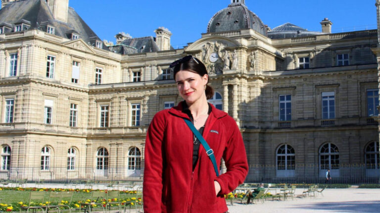 Writer Betty in a red jacket stands in front of the Luxembourg Palace in Paris