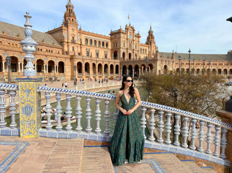 Writer Clara in a green dress stands on a bridge at Plaza de España